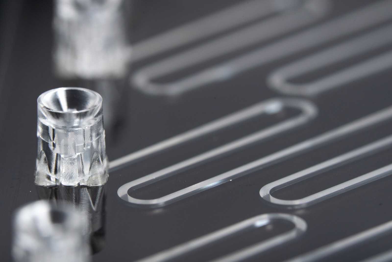 A microfluidic device with multiple pipette interfaces connected to a zig-zagging channel. The device is placed on top of a black background.