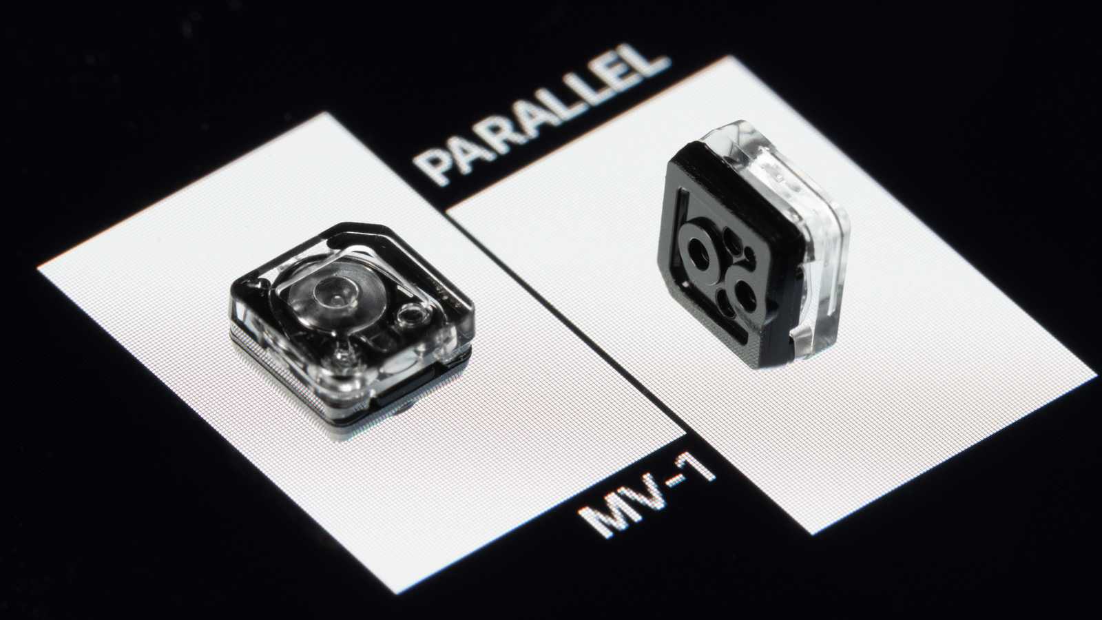Two MV-1 microvalves. The left microvalve is facing up with its circular diaphragm visible through its transparent top housing. The right microvalve is standing on its side with three ports visible on the black bottom housing.