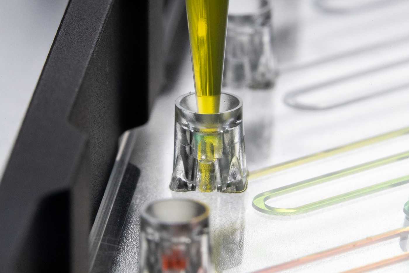 A 200 μL pipette tip engaging with Parallel's pipette interface, dispensing yellow fluidic into the channel.